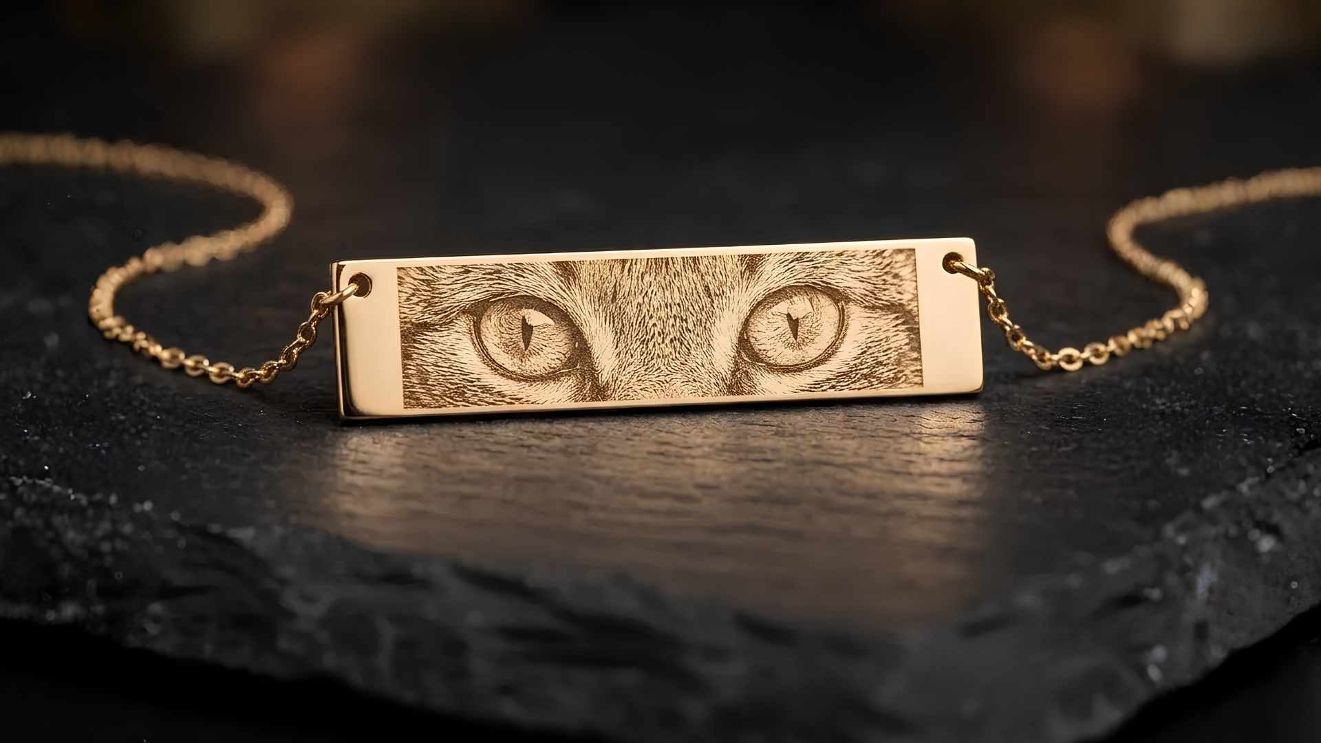 Close-up of engraved eyes on a gold bar pendant, showing pupil and lash detail