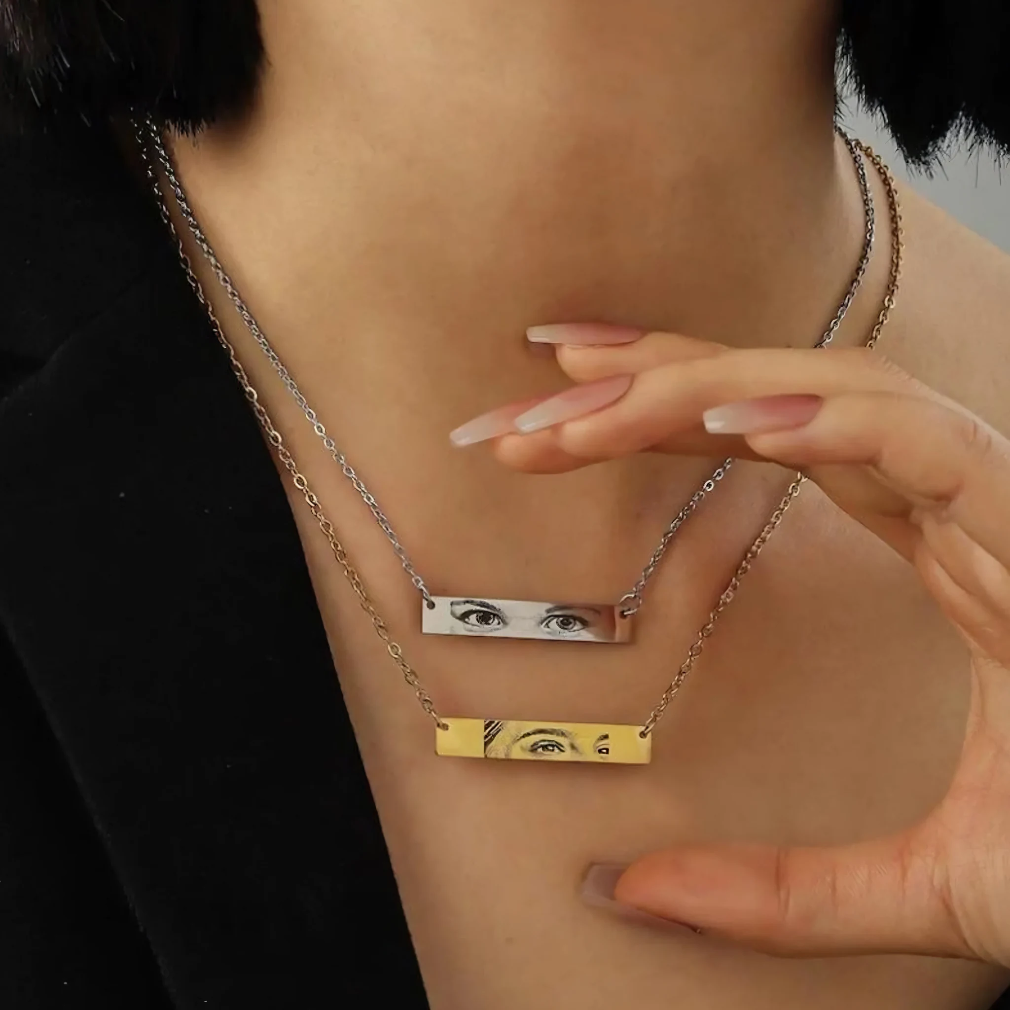 Woman wearing two layered Held Gaze bar-pendant necklaces, silver and gold, each engraved with a different pair of eyes